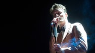 Sänger der Band Efterklang im weißen Anzug mit Fliege singt mit geschlossenen Augen ins Mikrofon