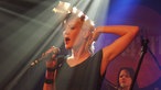 Die Frontfrau von AK4711 steht bei Bootleg im April 2006 im Scheinwerferlicht und greift sich an den Hinterkopf.
