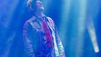 Mann mit roter Krawatte und Jeansjacke  in blauem Licht auf der Bühne