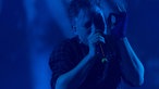Sänger in dunklem Bühnenlicht beim singen ins Mikrofon mit gefühlvoller Fingergeste