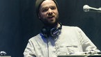 Mann mit Wollmütze, Vollbart und Kopfhörern um den Hals