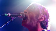 Der Sänger von Naked Lunch singt mit weit geöffnetem Mund in das Mikrofon.