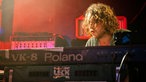 Hinter seinem Keyboard guckt eines der Bandmitglieder gerade so hervor, während er mit dem spielen beschäftigt ist.