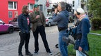 Der Sänger der Band und der Moderator des Rockpalastes stehen vor der Kamera am Straßenrand und werden gefilmst.