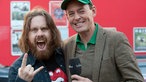 Der langhaarige und bärtige Frontmann der Band Monster Truck steht mit dem Moderator des Rockpalastes auf der Straße.