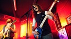 Die Beiden Männer mit den Saiteninstrumenten sind aus dem Publikum heraus zu sehen , während der Sänger der Band in das Mikrofon zu schreien scheint.