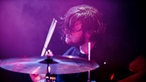 Ein seitlicher Blick auf den Drummer, dem beim Spielen die Haare ins Gesicht fallen. Er wirkt versunken.