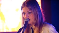 Kill It Kid Sängerin Stephanie Ward. Sie singt, den Mund dicht am Mikro, und schenkt der Kamera einen intensiven Blick.