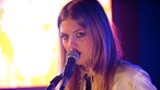 Kill It Kid Sängerin Stephanie Ward. Sie singt, den Mund dicht am Mikro, und schenkt der Kamera einen intensiven Blick.