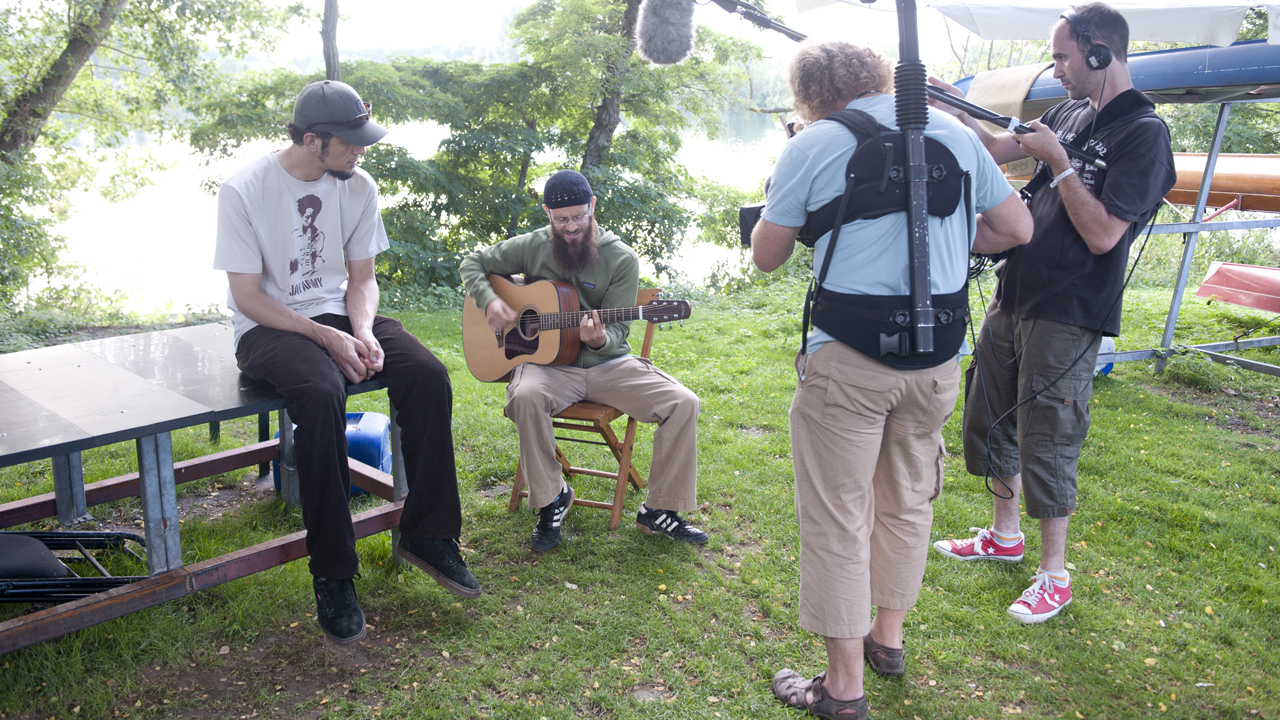 Groundation unplugged auf einer Wiese auf Holzstühlen während ein Kamerateam aufnimmt