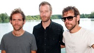 Die Band "The National" steht nebeneinander am Ufer eines Sees
