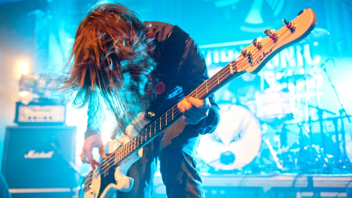 Bassist spielt mit angewinkelten Beinen, nach vorne gebeugt im blauen Licht