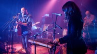 Vorne spielt die junge Frau ein Glockenspiel und im Hintergrund sieht man Honig singen