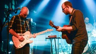 Sänger und Gitarrist der Band Honig stehen sich gegenüber und spielen sich heiße Töne zu