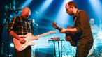Sänger und Gitarrist der Band Honig stehen sich gegenüber und spielen sich heiße Töne zu