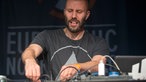 Mann mit Glatze und Bart dreht an Knöpfen auf einem Mischpult