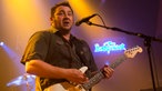 Gitarrist von King King spielt einen Akkord, singt ins Mikro und schaut vermeintlich ins Publikum