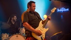 Gitarrist von King King spielt ein heißes Solo auf seiner weißen Fender Stratocaster Gitarre, im Hintergrund ist das Rockpalast Logo zu sehen
