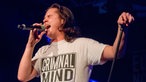 Lukas Graham singt mit zugekniffenen Augen und hält den Mikrofonständer mit einer Hand von sich weg