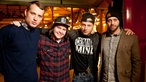 Vier Bandmitglieder von Lukas Graham stehen Arm in Arm nebeneinander