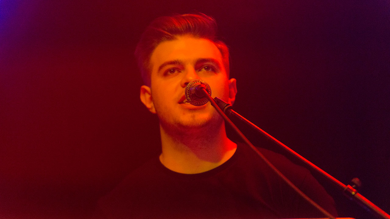 Frontmann von New Desert Blues singt geradeweg ins Mikrofon hinein, Frisur lässig nach hinten