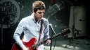 Noel Gallagher guckt während dem Gitarre spielen grübelnd nach unten.