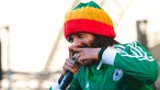 Protoje macht ein zeigefinger Zeichen beim singen