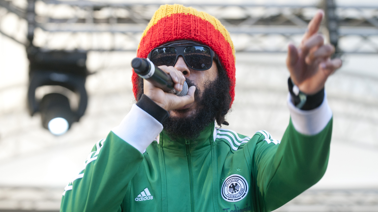 Protoje mit Mütze und Trainingsjacke zeigt ins Publikum und singt