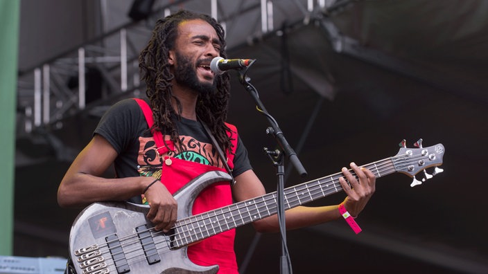 Bassist Delroy Hamilton steht am Mikrofon, spielt sein Instrument und singt.