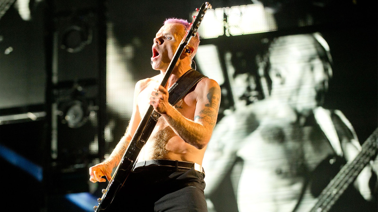 Gitarrist in einer wilden Pose mit seiner Gitarre; im Hintergrund sieht man eine Projektion von ihm in schwarz weiß
