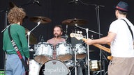 Gitarrist und Bassist von Dispatch auf der Bühne dem Schlagzeuger zugewandt