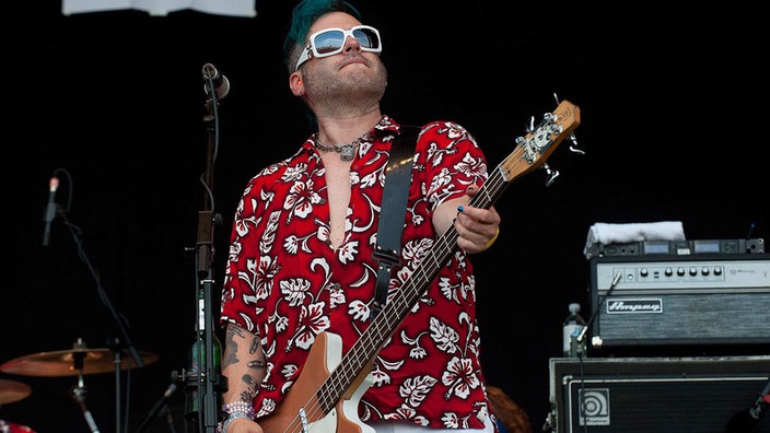 Bassist posiert und schaut Richtung Himmel, trägt ein schönes Hawaiihemd und einen 3-Tage-Bart