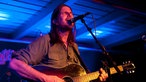 Jonathan Wikson steht mit seiner Akustikgitarre singend auf der Bühne.