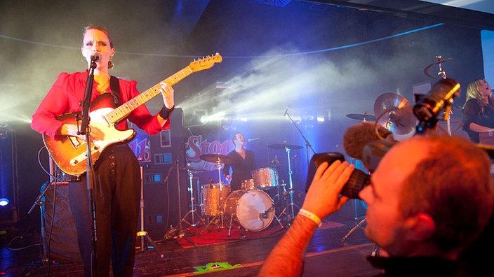 Im rechten Vordergrund steht ein Kameramann, der Anna Calvi fotografiert während auf der linken Seite eben diese performt.