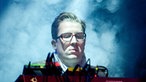 Der Keyboarder von Wilco sieht konzertriert nach unten auf sein Instrument während er von oben weiß angestrahlt wird.