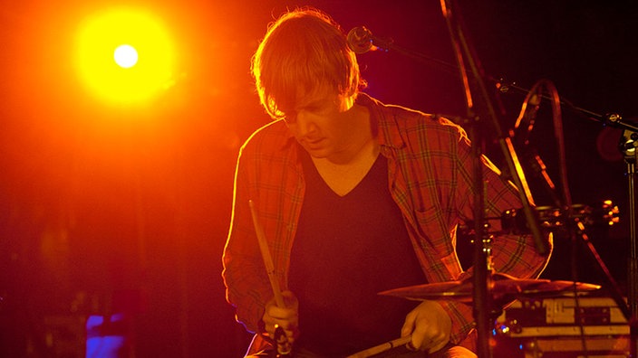 Der Drummer der Band An Horse wird von hinten orange angestrahlt.