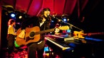 Der Sänger der Other Lives steht neben einem Klavier mit einer Gitarre in der Hand und singt.
