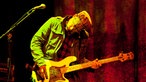 Der Bassist der Band Cake beugt sich gerade während des spielens nach vorne über.