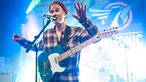 Sänger mit umgehängter Gitarre singt mit gehobenen Händen 
