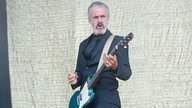 Mann im schwarzen Anzug spielt Gitarre und schaut ernst zur Seite