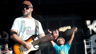 Gitarrenspieler im Vordergrund, klatschendes Bandmitglied im Hintergrund
