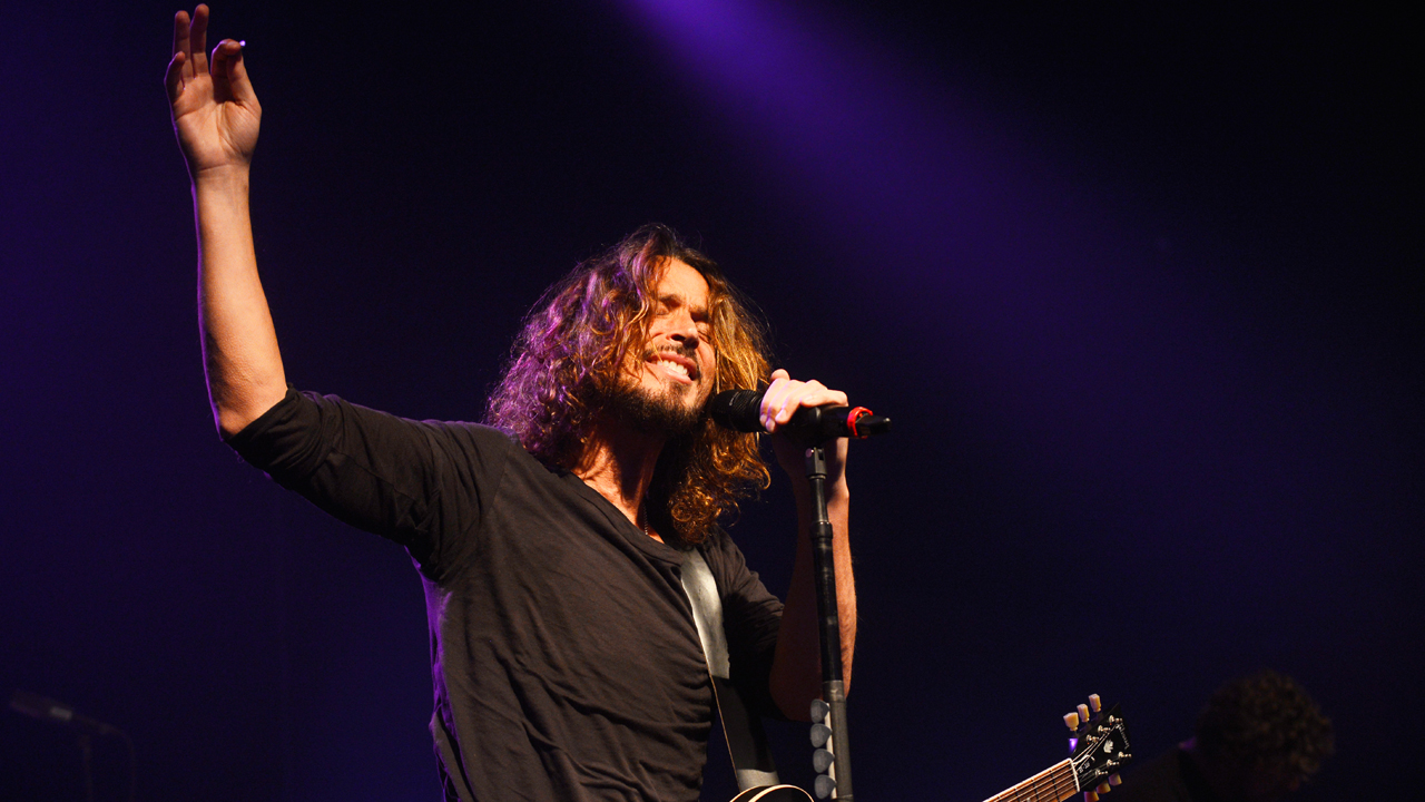 Der Sänger von Soundgarden hält sich mit der linken Hand am Mikrofon fest und streckt die Rechte in die Höhe.