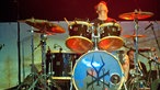 Der Drummer sitzt hinter seinem Schlagzeug und sieht in die Höhe.