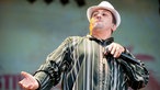Frontmann Hakim Meridja posiert mit weissem Hut und Mikrofon auf der Bühne des Summerjam. Er streckt die rechte Hand aus und zeigt einen einstudierten, arroganten Blick 
