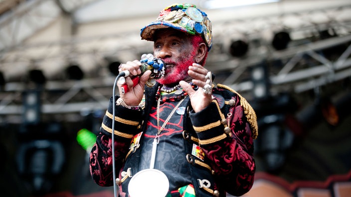 Lee "Scratch" Perry blickt von der Bühne, um den Hals eine grosse schwere Kette, ähnlich der Uhr von Jam Master Jay (Run DMC)