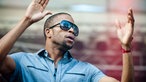 "Trombone Shorty" hebt beide Arme in die Luft und hat den Mund leicht geöffnet