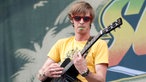 Gitarrist mit roter Sonnenbrille und Plektrum im Mund