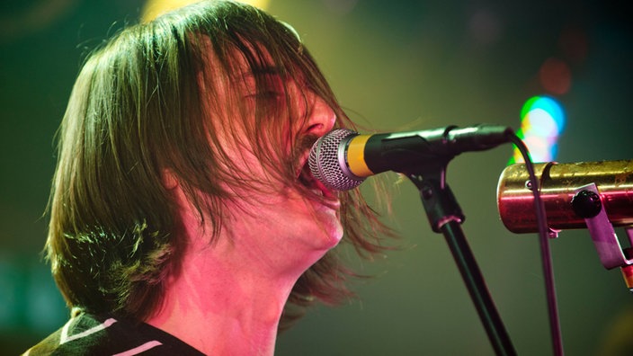 Der Sänger von "The Datsuns" singt in ein Mikrofon, im sind die Haare ins Gesicht gefallen