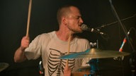 Drummer spielt Schlagzeug und singt mit geschlossenen Augen in ein Mikrofon