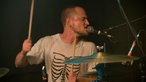 Drummer spielt Schlagzeug und singt mit geschlossenen Augen in ein Mikrofon